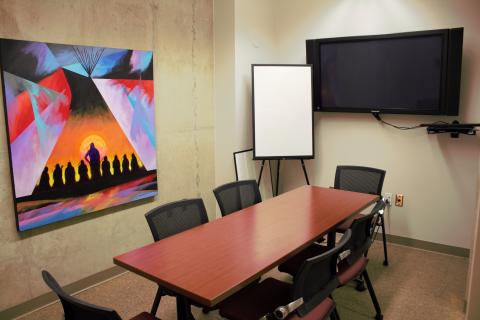 Meeting room with a table, 6 chairs, and a display screen on the wall